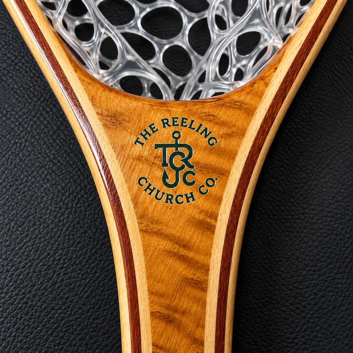 Close-up of a wooden paddle or handle with a silver open-weave top, featuring an engraved logo that reads 'THE REELING CHURCH CO.' on a black textured background.