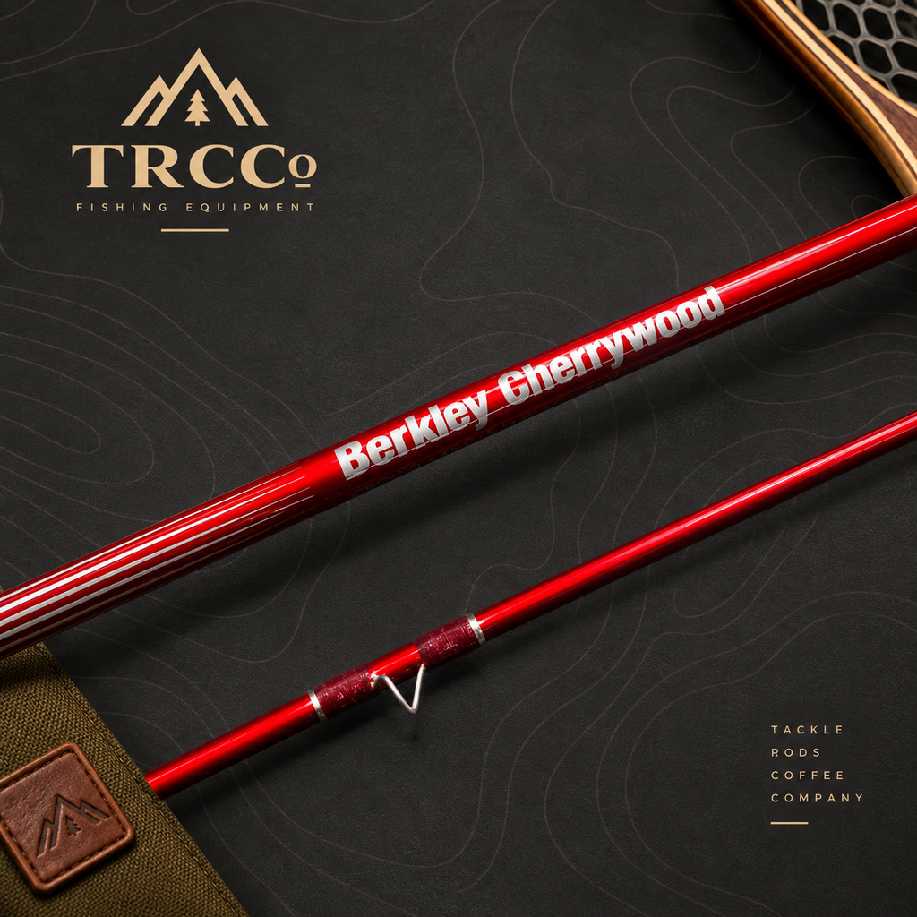 A close-up product shot of a red fishing rod section with white text reading 'Berkley Cherrywood' and a visible TRCC logo in the upper left. The rod is laid diagonally on a dark textured background with topographic contour lines, plus a small brown leather strap and part of a wooden accessory at the top right.